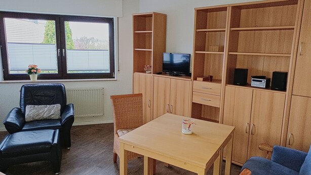 A furnished room with a black leather chair, a wooden table, a television on a shelf, and a large wooden cabinet.