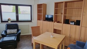 A furnished room with a black leather chair, a wooden table, a television on a shelf, and a large wooden cabinet.