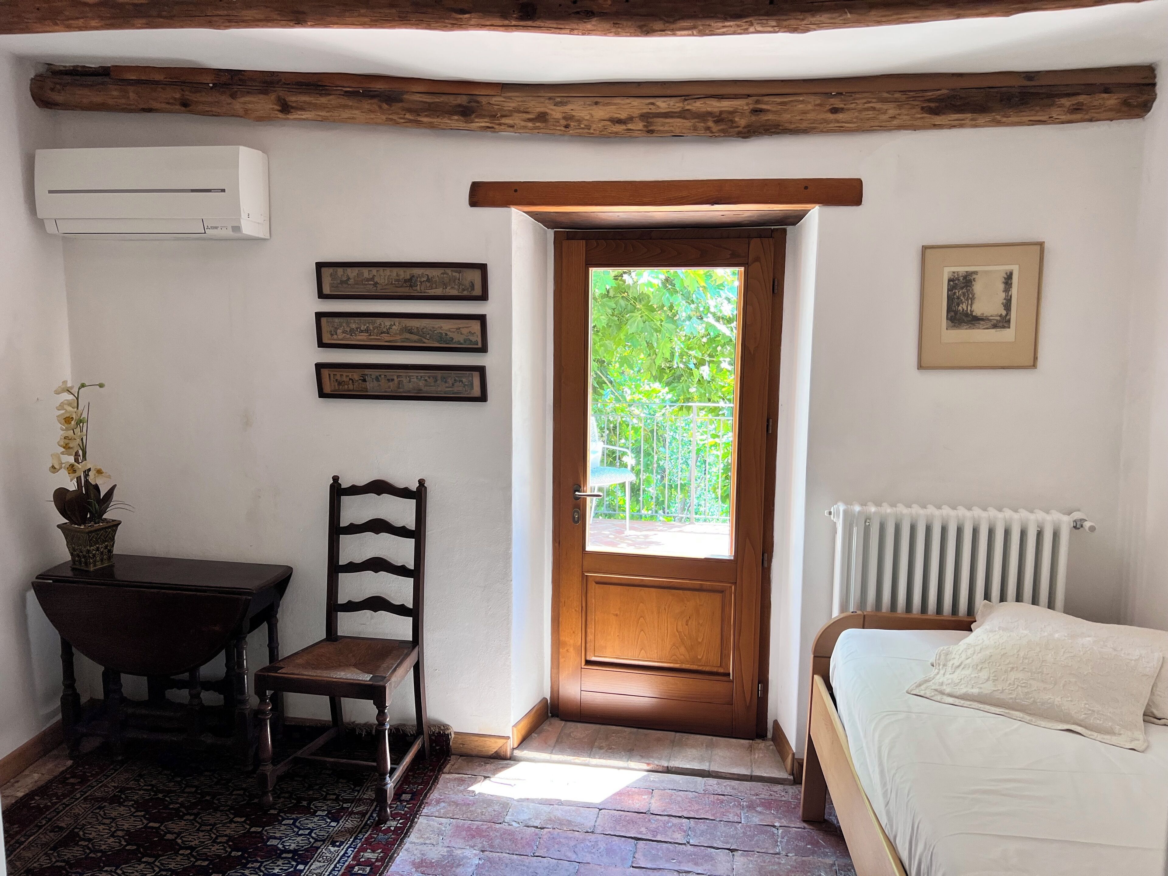 Une pièce comprenant un lit, une chaise, une table, un radiateur et une porte donnant sur un balcon.