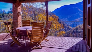 Un espacio de estar al aire libre techado con mesa y sillas, con vistas a un paisaje montañoso con follaje otoñal.