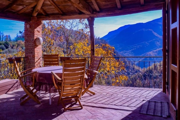 Un espace extérieur abrité, avec une table et des chaises, offrant une vue sur un paysage montagneux aux couleurs automnales.