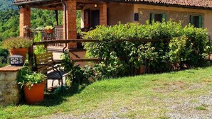 Una villa rústica con techo de tejas, un porche cubierto y abundante vegetación.