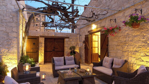 An outdoor patio with wicker furniture, stone walls, and a wooden door. - Sanders Arsorama - Sweet 1-bdr Apt w/ Shared Patio (Arsos)