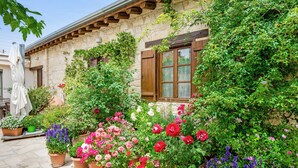 A stone building with a wooden balcony and a window with shutters. There are potted plants with flowers in front of the building. - Sanders Arsorama - Sweet 1-bdr Apt w/ Shared Patio (Arsos)