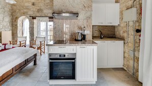 A compact kitchen with a built-in oven, white cabinetry, and a stone wall backdrop. - Sanders Arsorama - Sweet 1-bdr Apt w/ Shared Patio (Arsos)