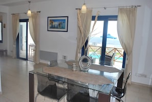 A dining area with a glass table, chairs, a decorative mirror, and a view of the sea. - Sea Front Villa, Heated Private Pool, Amazing Location Paphos 323 (Kissonerga)