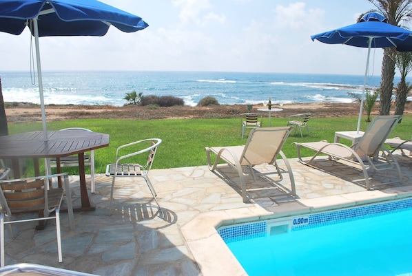 A pool area with a view of the ocean, outdoor seating, and a stone patio. - Sea Front Villa, Heated Private Pool, Amazing Location Paphos 323 (Kissonerga)