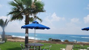 Een terras met een tafel en stoelen, een blauwe parasol en uitzicht op de oceaan.