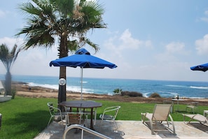 A patio with a table and chairs, a blue umbrella, and a view of the ocean.