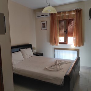 A neatly made bed in a hotel room with a headboard, a bedside table with a lamp, a window with blinds, and an air conditioning unit on the wall. - Villa Stefanos, Sea View, Private Pool, Near Sea (Rethymno)