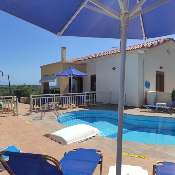 A swimming pool with blue tiles, surrounded by lounge chairs and a covered area with a blue umbrella. - Villa Stefanos, Sea View, Private Pool, Near Sea (Rethymno)