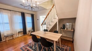 Ein Essbereich mit Holztisch, zwei Stühlen, einer Chandelierleuchtre, einer Treppe und einem kleinen Regal mit einem gerahmten Bild und einer Tasse.