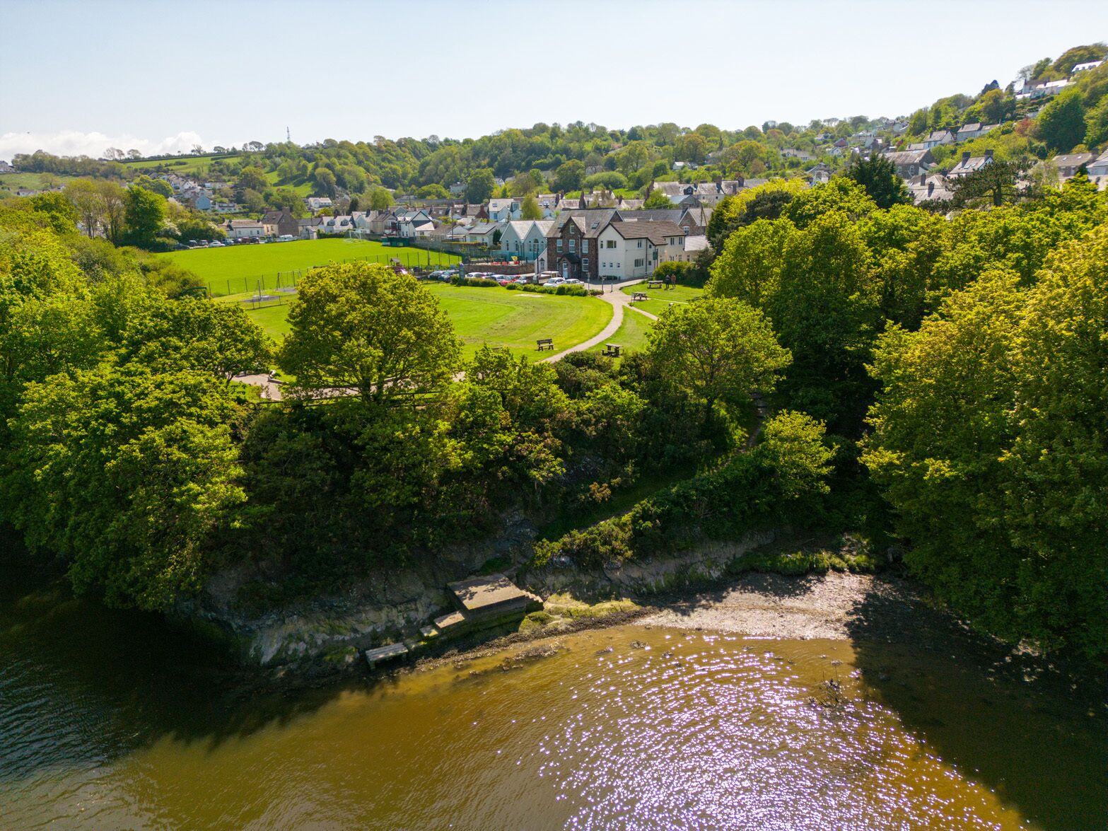 A riverside view of a residential area with houses, a park, and a large building.