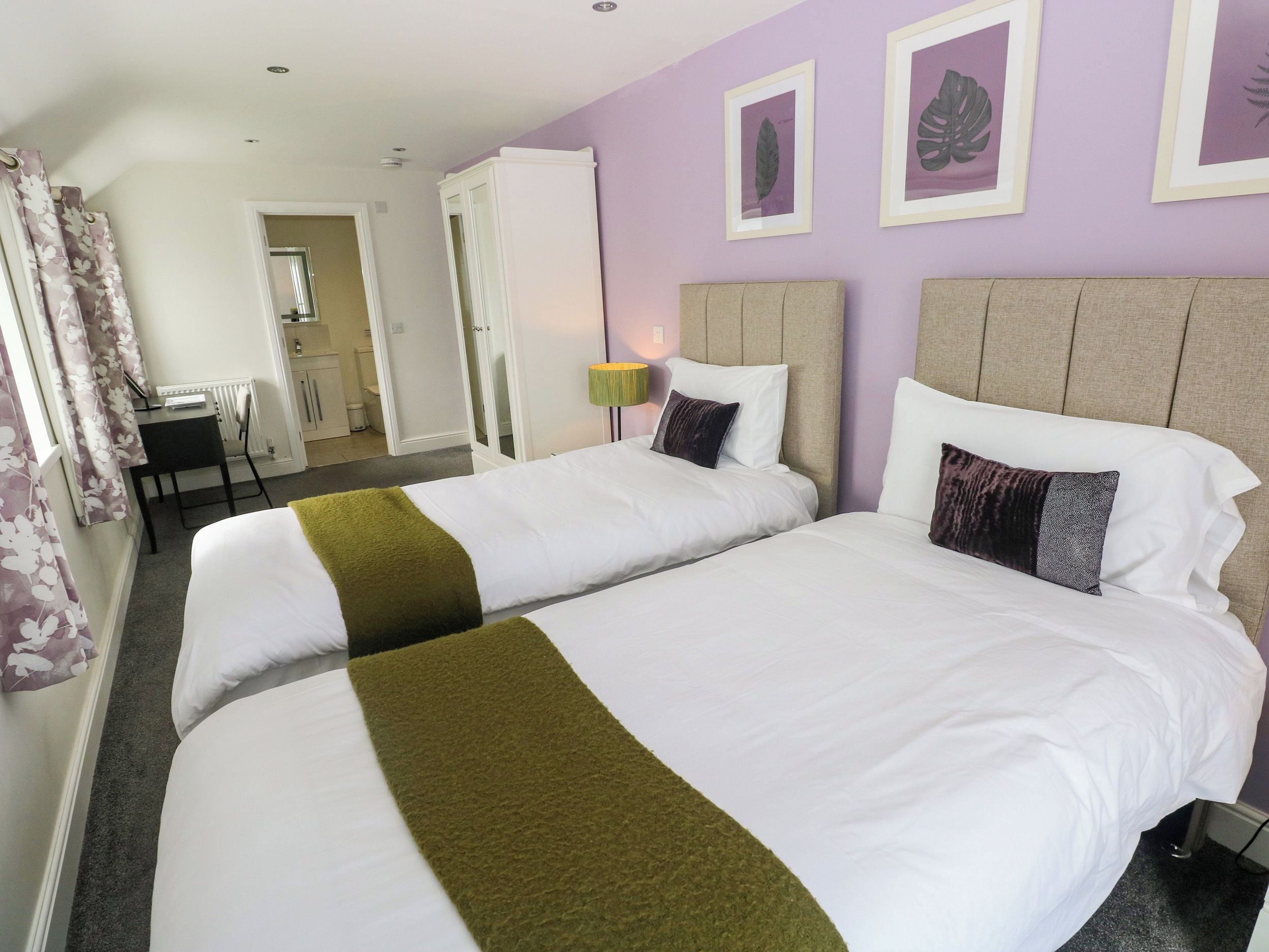 A hotel room with two beds, a desk, and a bathroom visible in the background.