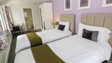 A hotel room with two beds, a desk, and a bathroom visible in the background.