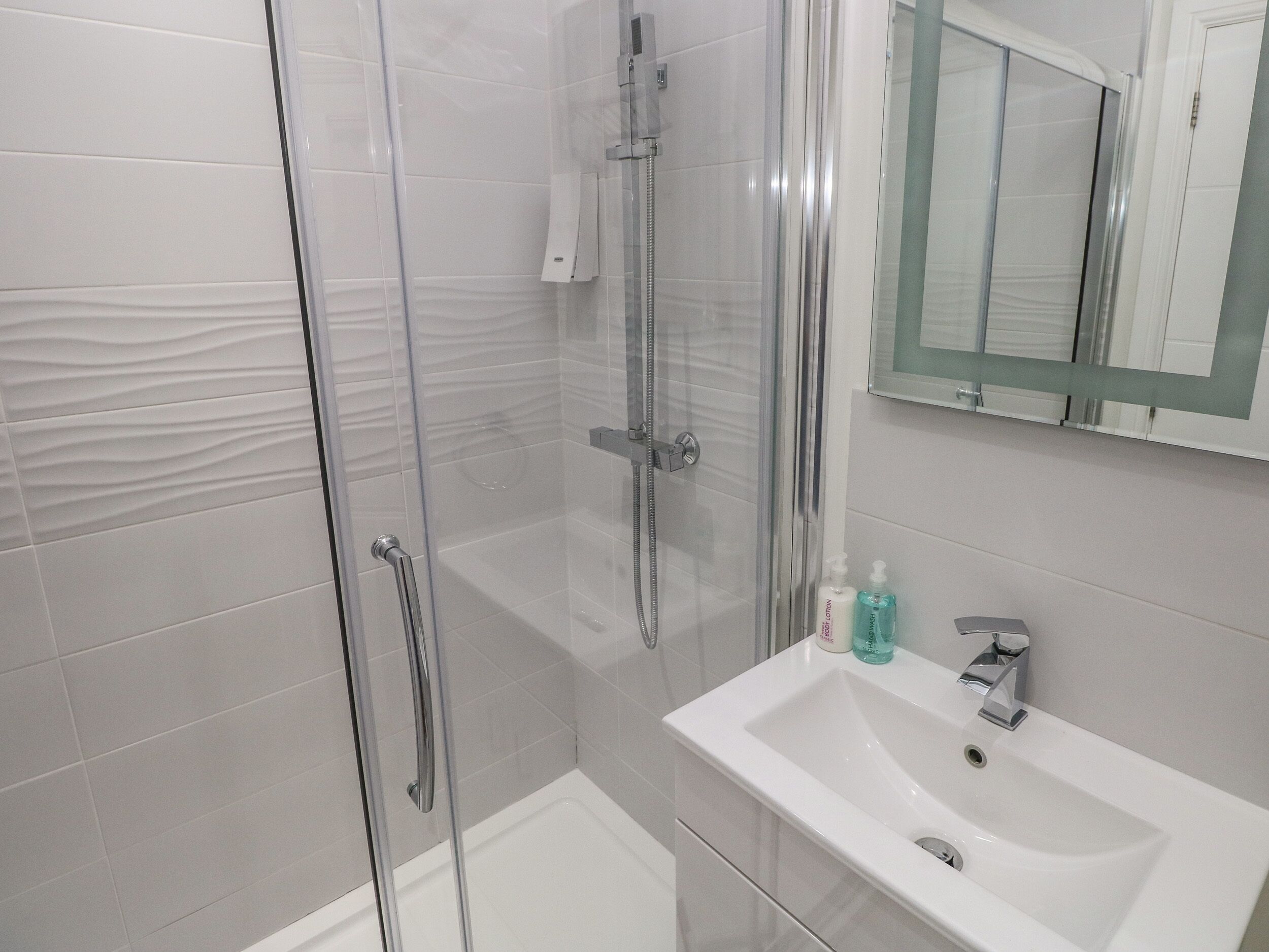 A modern bathroom with a glass shower enclosure, a white sink, and a mirror above it.