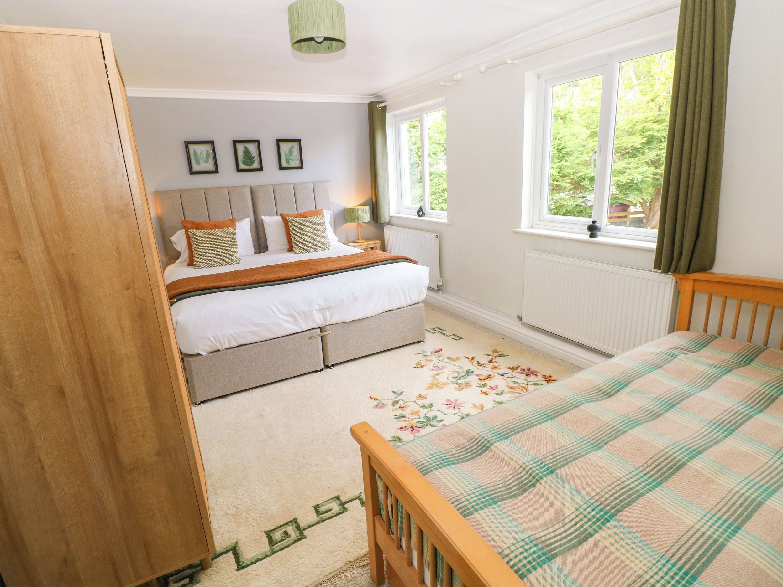 A bedroom with a bed, a dresser, a window with curtains, and a radiator.