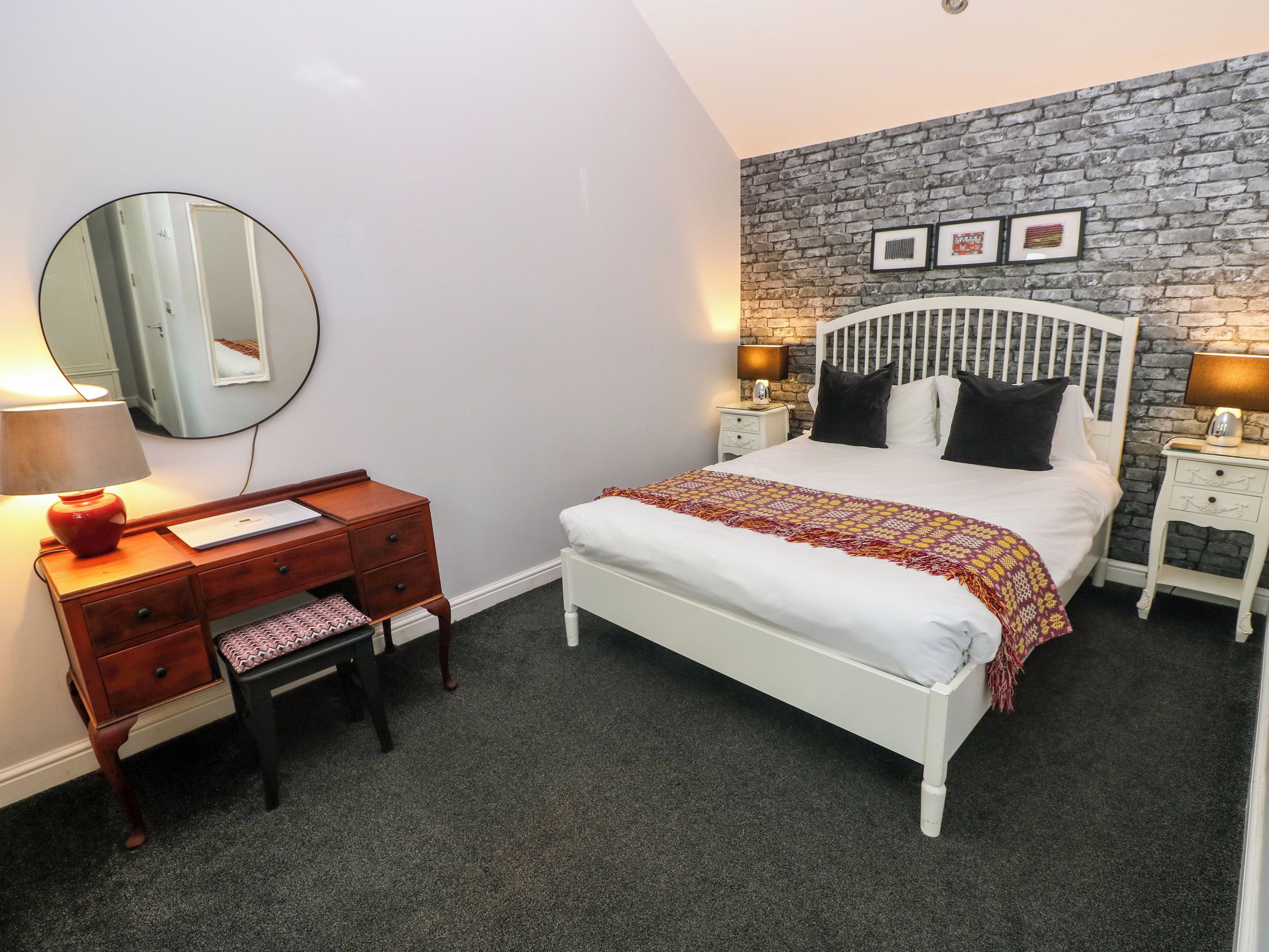 A bedroom with a bed, a dresser, a mirror, and a wall with a brick pattern.