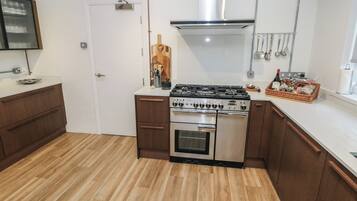 Cocina compacta con estufa a gas, horno y campana extractora de acero inoxidable. Cuenta con armarios de madera, encimera blanca y una puerta con picaporte.
