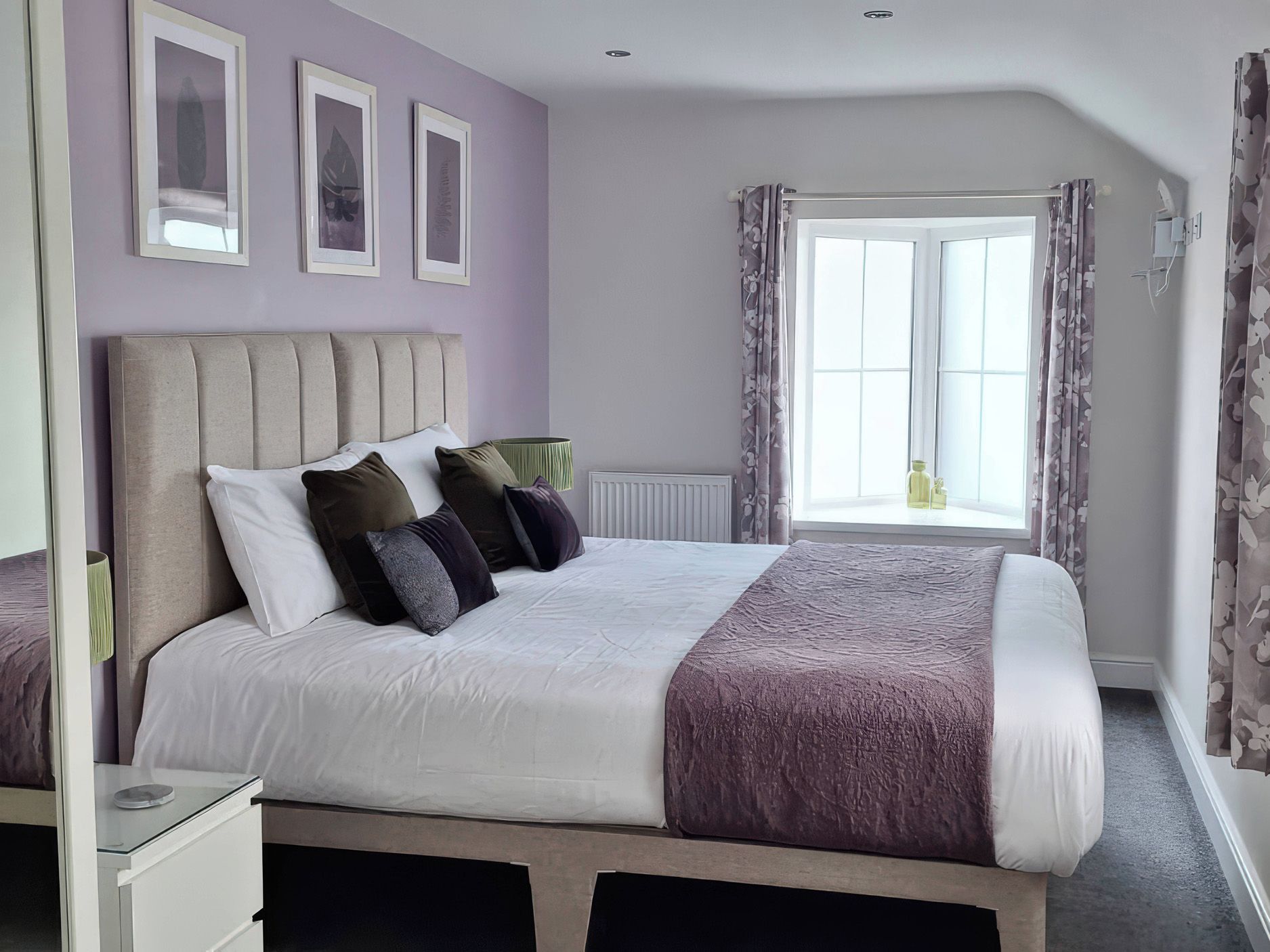 A bedroom with a large bed, a window with curtains, and a radiator.