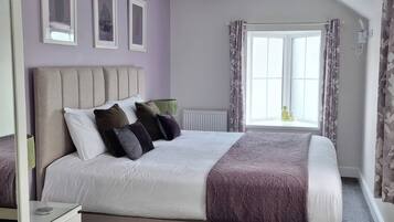 A bedroom with a large bed, a window with curtains, and a radiator.