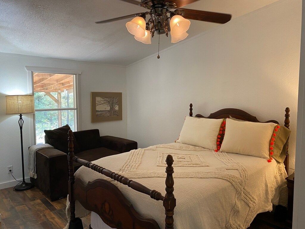 A bedroom with a four-poster bed, a ceiling fan, and a window with a view of trees.