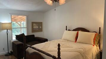 A bedroom with a four-poster bed, a ceiling fan, and a window with a view of trees.
