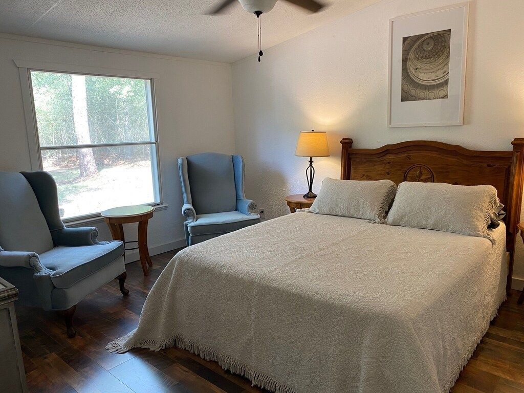 Une chambre à coucher avec un lit, deux chaises, une table de chevet, une lampe et une fenêtre.