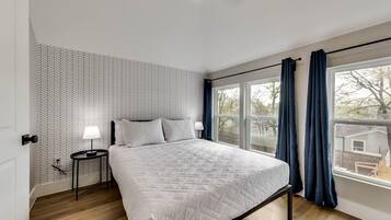 A bedroom with a bed, a nightstand, a window with curtains, and a patterned wall.