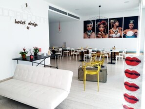 A modern hotel lobby with a white sofa, yellow chairs, and a dining area with white chairs and tables. - Copacabana Hotel Design (Margherita di Savoia)