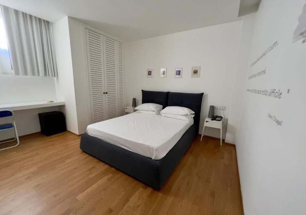 Ein Schlafzimmer mit einem Bett, einem Schreibtisch, einem Stuhl, einem Kleiderschrank und einer Wand mit gerahmten Bildern.