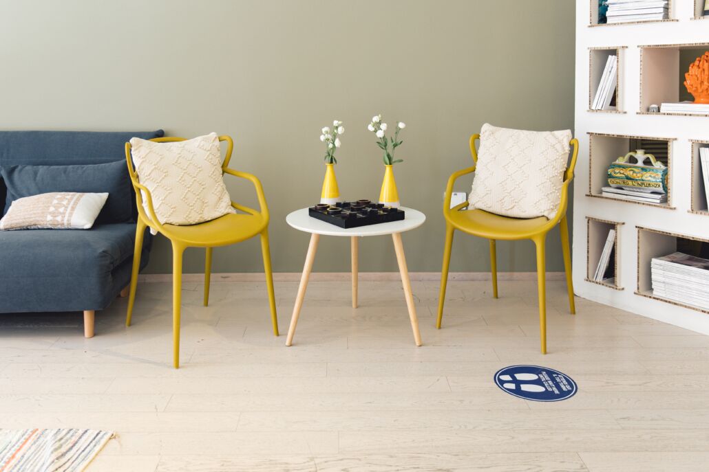 A room with a blue sofa, two yellow chairs, a small round table with vases, and a bookshelf.