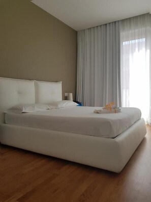 A large bed with white linens in a room with wooden flooring and a neutral-colored wall. - Copacabana Hotel Design (Margherita di Savoia)