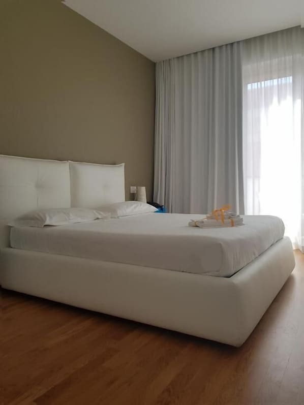 Ein großes Bett mit weißen Leinen in einem Zimmer mit Holzboden und einer Wand in neutralen Farben.