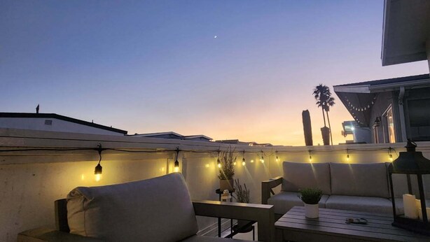 A rooftop terrace with a sofa, a table, and string lights. - Peek-A-BOO ocean view. 50 Steps to the Sand Large Remodeled Beach House.  (Newport Beach)
