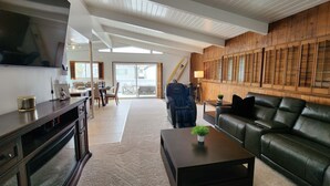 A spacious living room with a large flat-screen TV, a leather sofa, a coffee table with a plant, and a dining area with a table and chairs. - Peek-A-BOO ocean view. 50 Steps to the Sand Large Remodeled Beach House.  (Newport Beach)