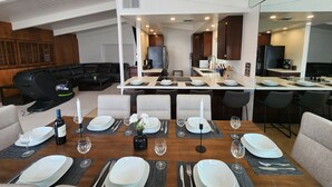 A modern living room with a black leather sofa, a dining table set for six with white plates, glasses, and a bottle of wine. - Peek-A-BOO ocean view. 50 Steps to the Sand Large Remodeled Beach House.  (Newport Beach)