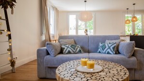 Un salón con un sofá azul, una mesa de centro redonda de madera y dos vasos de jugo de naranja.