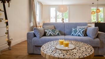 A living room with a blue sofa, round wooden coffee table, and two glasses of orange juice.