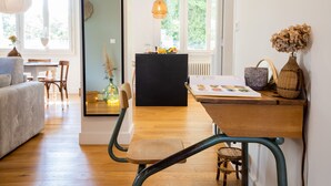 Una sala de estar acogedora con un sofá, una mesa de comedor de madera y sillas. Se observa un mueble negro con objetos decorativos y una ventana que ofrece vistas a zonas verdes.