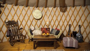 Una habitación acogedora con piso de madera, un sofá con cojines, una mecedora de madera, una mesa pequeña con una cesta de fruta, una guitarra y un tambor.