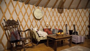 Una habitación acogedora con una mecedora de madera, un sofá, una mesa con fruta y guitarras frente a una pared con celosías.