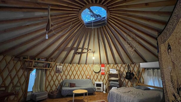 Una yurta con techo de madera circular, un sofá, una pequeña mesa y una cama.
