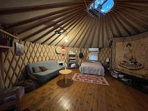 Interieur van een joert met een houten spantwand, een bed, een bank, een kleine tafel en een hanglamp.