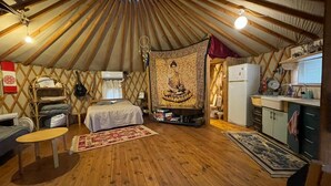 Una yurta con una cama, una pequeña mesa, una zona de cocina y un tapiz.