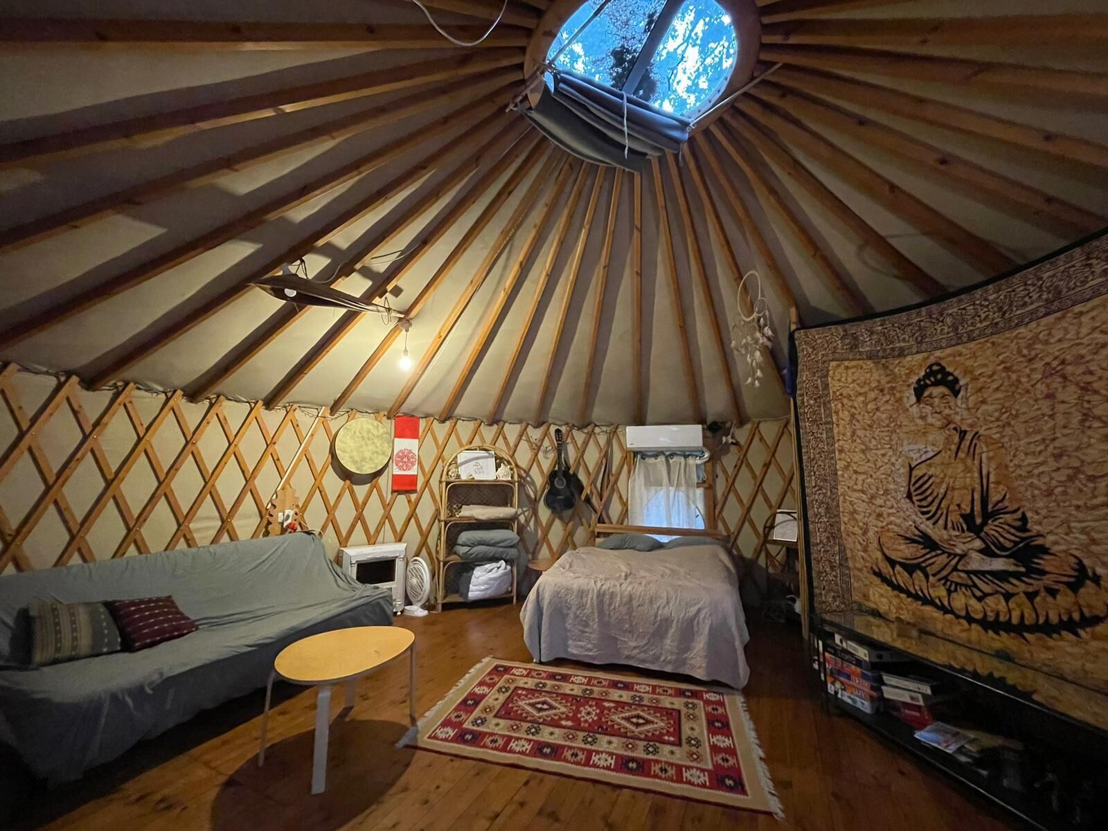 Eine Jurte mit Bett, Sofa, kleinem Tisch, Heizung und Wandteppich.