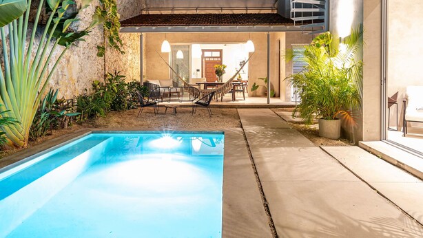 A modern outdoor pool area with a concrete deck, surrounded by tropical plants and a stone wall. - The Horseshoe - spacious pool & sunset roof terrace (Mérida)
