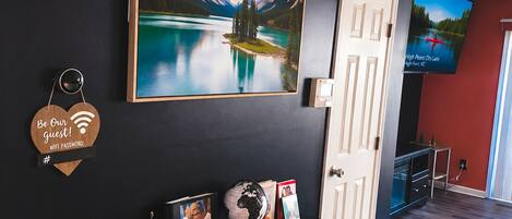 Ein modernes Interieur mit einer schwarzen Wand, einem großen gerahmten Landschaftsbild, einer weißen Tür und einem flachbildschirmfernseher, der darüber angebracht ist.