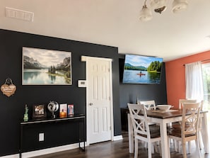 A dining area with a table and chairs, a television mounted on the wall, and a door. - 2BR · High Point · Hickswood Townhome (High Point)