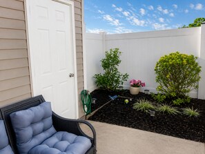 Un espace patio avec une porte blanche, une chaise en osier et diverses plantes.